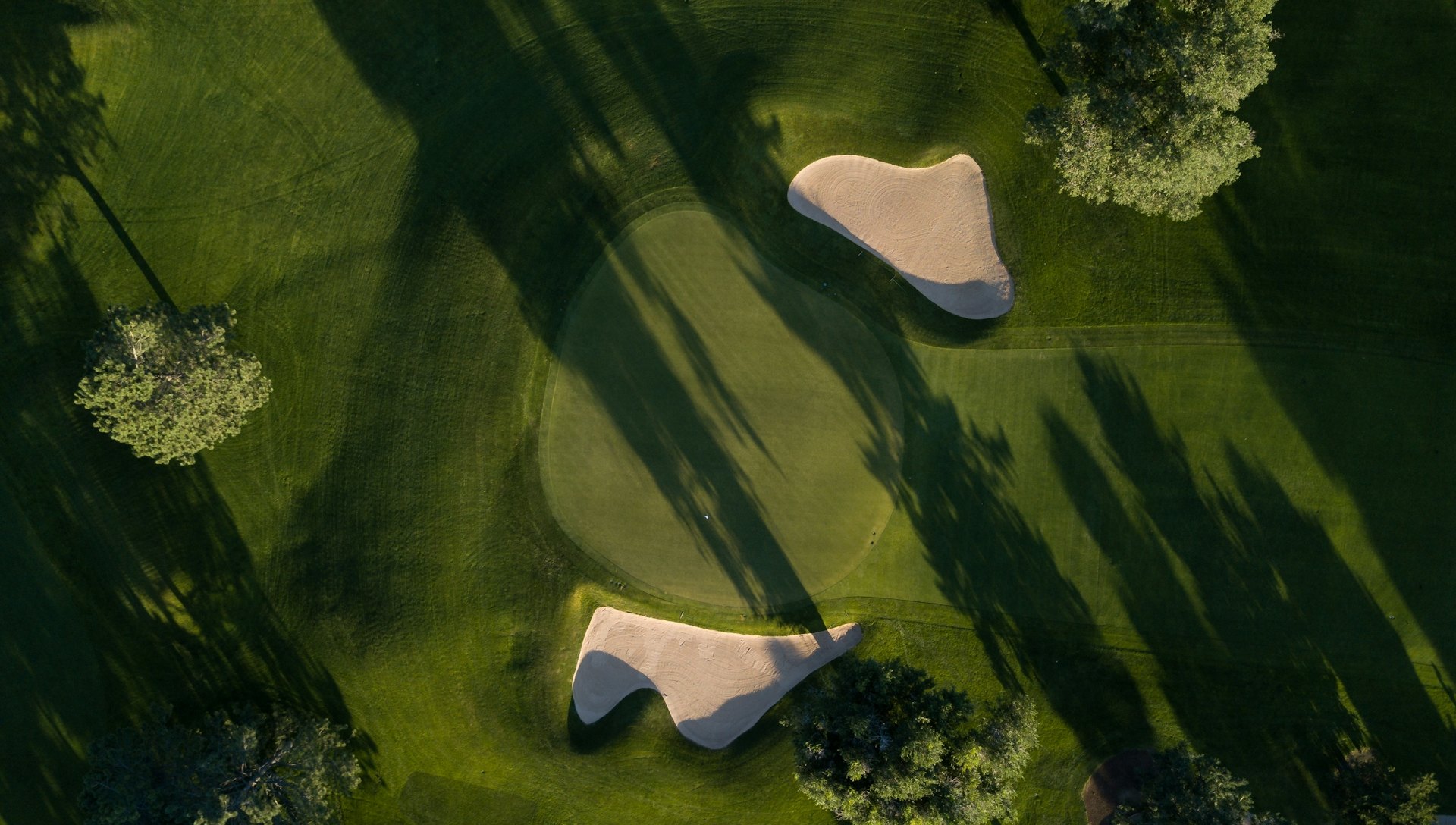 Aerial view of a golf course green framed by bunkers and mature trees
